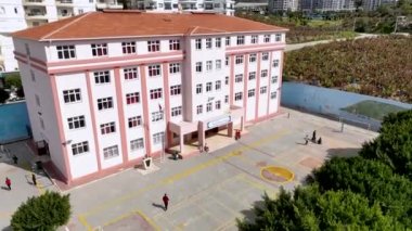 Güneşli bir günde okul, İHA düzgün bir şekilde sağa doğru hareket ediyor, çocuklar futbol oynuyor..