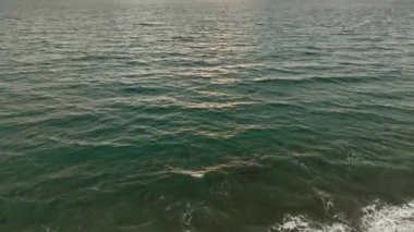 Okyanus zarafetine tanık olun. Sinematik dronumuz büyüleyici deniz manzarasını ve desenli dalgaları dramatik bulutlu günbatımında sergiliyor..