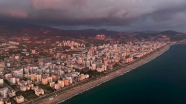 Sihirli altın saatimize tanık olun. Sinematik dronumuz büyüleyici Akdeniz kıyısında gün batımını sergiliyor. Şehirde büyüleyici bir parıltı yayıyor.