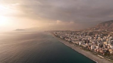 Alacakaranlık zerafetinin tadını çıkartırken sinematik dronumuz denizin üzerindeki yumuşak tonlarda zarif günbatımını yakalar ve şehir manzarasıyla uyumlu bir görsel senfoni yaratır..