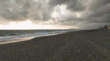 Bir kış fırtınasının görkemli gücüne tanık olun. İnsansız hava aracı dokulu denizi yakalıyor. İnsanlar sakin plajda, canlı günbatımında yavaşça geziniyor..