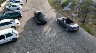 İnsansız hava aracı eski bir kalenin kıvrımları ve virajlarından geçen üstü açık bir arabanın izini sürerken yeşil ağaçların yol boyunca çizdiği heyecan verici hava macerası.