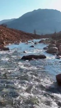 Kayalık bir arazide akan sular gibi kendini bir nehrin ihtişamına daldır. Bu dikey video dramatik manzarayı ve dinamik enerjiyi yakalar ve onu nefes kesici bir canlı yapar.