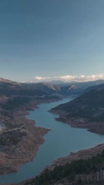 Gün batımında nehrin üzerinde kule gibi yükselen dağların ihtişamını bu dikey videoda tecrübe edin. Sıcak renkler ve dramatik manzaranın ekranınızı nefes kesici bir duvar kağıdına dönüştürmesine izin verin..