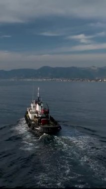 Akdeniz 'deki üssüne giden bir deniz römorkörünün zarif dönüşüne tanık olun. Bu dikey video mavi denizin güzelliğini yakalar römorkör sakin sularda zahmetsizce ilerlerken.