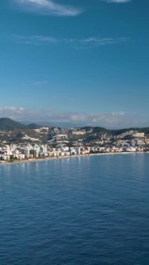 Bu dikey videoda dron hızla kıyıya doğru uçarken deniz kenarı boyunca şehri keşfedin. Kendini kentsel ve doğal güzelliklerin karışımına ver.