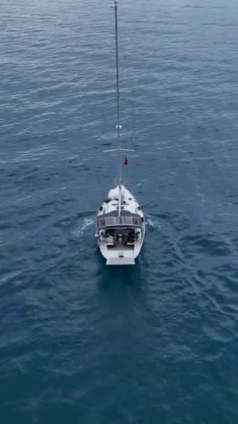セーリングヨットの静けさを体験してください この垂直方向のビデオでは ゆっくりと帆で港に入ります 壮大な深海の背景と瞬間の静けさを賞賛する — ストック動画