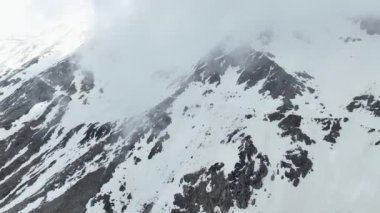 İlk baharın gizemli hava keşfine çıkın. Büyüleyici dağ manzarası. İHA, kar tozlu zirvelerin ve göksel bulutların sinematik görüntülerini yakalar..