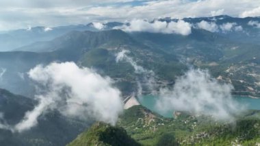 Kendinizi havanın büyüleyici güzelliğine daldırın, bulutlarla süslenmiş görkemli dağ manzarasını ve aşağıdaki canlı yeşil ormanları göstererek.