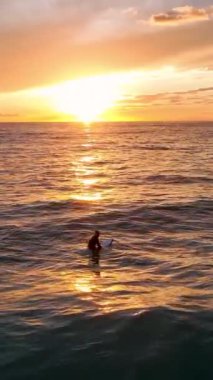 Gün batımı dalgalarının destansı güzelliğine tanık olun. Sörfçüler günün son dalgalarını sürüyorlar. Bu dikey videoda çarpıcı görüntüler yaratıyorlar..