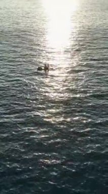 Gün batımı yansımaları sırasında suda sürüklenen sportif bir çiftin dinginliğini hissedin büyüleyici bir hava perspektifinden yakalanırlar..