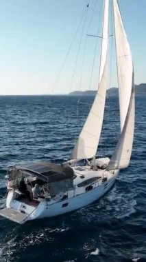 Bir yatın büyüleyici Akdeniz kıyısındaki limana doğru yelken açması gibi bir deniz yolculuğunun zarafetini yaşayın. Bu dikey videoda sinematik bir yetenekle filme alınmıştır..