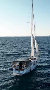 Bir yat zarif bir şekilde Akdeniz limanına doğru yelken açarken açık denizlere kaçmak, bu dikey videoda havadan çekilmiş bir görüntü..