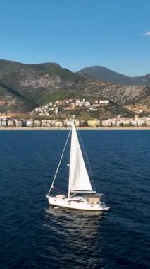 Bir yelkenlinin büyüleyici Akdeniz kıyı şeridinde limana doğru ilerlemesinin mucizesini yaşayın. Bu dikey videoda nefes kesici hava görüntülerini yakalayın..