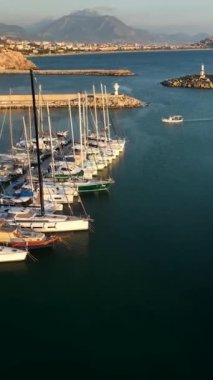 Bu dikey videoda, batan güneşin canlı renkleriyle süslenmiş Alanyas limanına demirlemiş yatların görkemli görüntüsüne hayret ediyorum..