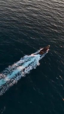 Kendinizi dingin güzelliğe daldırın. Lüks bir spor teknesi karanlık denizde gün batımında yol alırken yukarıdan çekilen bu dikey videoda....