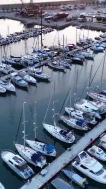 Deniz manzarası üzerinde süzülür ve günbatımında yatlarla süslenmiş Alanyas limanının görüntüsüne hayran kalır, bu dikey videoda sergilenir..