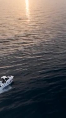 Deniz manzarasının üzerinde süzülür ve köpüklü izler bırakan beyaz bir teknenin görkemli deniz yolculuğuna hayran kalır ve bu dikey videoda sergilenen su yüzeyindeki canlı güneş ışığını yansıtır..