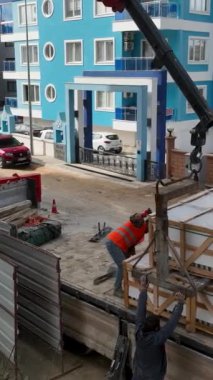 İnşaat alanının üzerinden yükselin ve bu dikey videoda inşaatçılar işlerini yaparken yükleri boşaltan bir vincin hava görüntüsüne tanık olun..