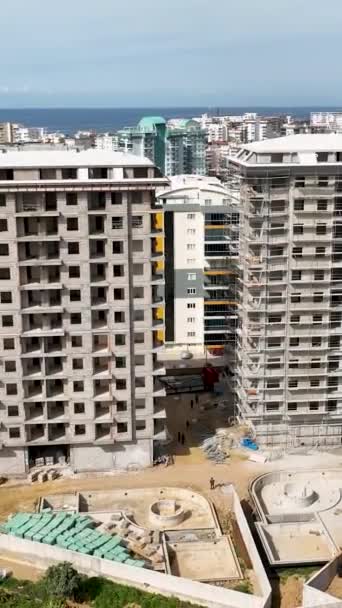 この垂直ビデオで上から賑やかな建物のサイトを観察すると 複数階建ての住宅プロジェクトの進捗状況を確認します — ストック動画