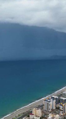 Fırtınalı Akdeniz kıyı şeridi ve şehir manzarası hakkında bilgi edinin. Bu dikey videodaki uyarının yoğunluğunu vurgulayın..