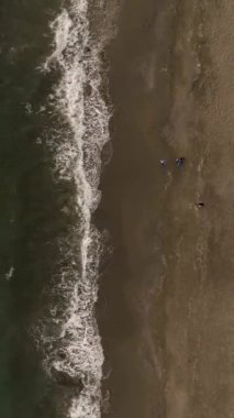 Büyüleyici günbatımının keyfini çıkarın. Sihirli bir plajda yürüyen ve bu büyüleyici dikey videoda havadan sakin bir ortam yakalayan insanlara tanık olun..