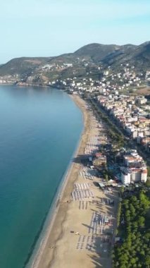 Temiz kum ve gök mavisi sularıyla pitoresk bir plajın üzerinde süzül, bu büyüleyici dikey videoda kendini mutlu bir sabah atmosferine daldır..