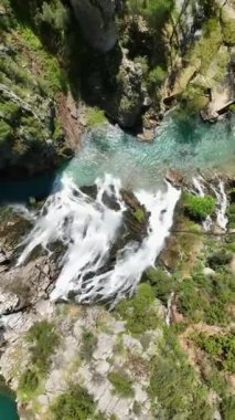 Tanınmış bir turist merkezindeki havadan bir şelalenin büyüleyici görüntüsünü ele alalım. Suyun zarif akışına ve yemyeşil suların bu dikey ortamda büyülü bir ortam yaratmasına izin ver.