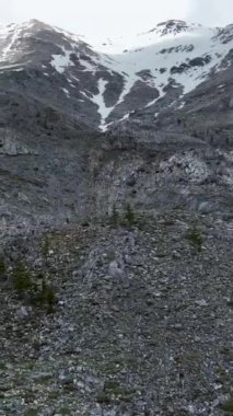 Karla kaplı dağların dramatik bulutlu gökyüzüne karşı hayranlık uyandıran güzelliğini hissedin. Dikey videonuzda nefes kesici hava görüntüsünü yakalayın.