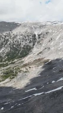 Görkemli dağların üzerinde süzülür, yüksek mevcudiyetlerini, karlı zirvelerini ve dramatik gökyüzünü gözler önüne serer. Dikey videonuzda nefes kesici hava görüntüsünün seyircilerinizi büyülemesine izin verin..