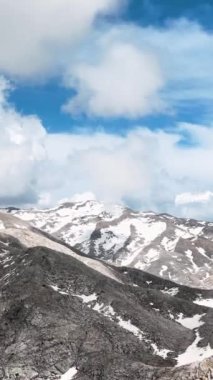 Görkemli karla kaplı zirveleri olan dağ manzarasının ilham verici güzelliğine tanık olun. Bu dikey videonun sizi nefes kesici manzaralar dünyasına götürmesine izin verin..