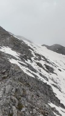Bulutların karla kaplı dağların tepelerinde dalgalanmasını, doğanın ihtişamını kutlayan büyüleyici bir hava manzarası yaratmasını hissedin..