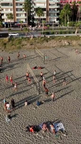 この垂直ビデオで上から沿岸のレクリエーションシーンを取ります ビーチ参加者がバレーボールの活発なゲームに従事し 楽しさと友情の雰囲気を作り出すように見てください — ストック動画