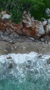 Kristal mavi dalgaların kayalık kıyıya çarpmasıyla el değmemiş bir kumsalın huzurunun tadını çıkarın..