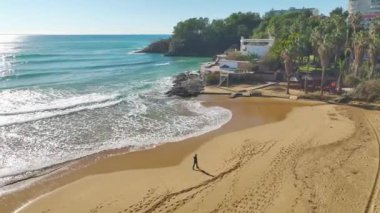 4K insansız hava aracı manzaralı, altın plajda yürüyen bir adamın sahnesini yakalayın. Yukarıdan Akdeniz kıyısının tadını çıkar..