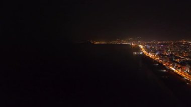 Karanlıkta parlayan neon ışıkları ve kuleleri olan parlak bir şehir manzarasına bakın..