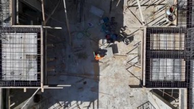 Demirleri büken ve temel için beton döken işçilerle dolu bir inşaat alanı görün..