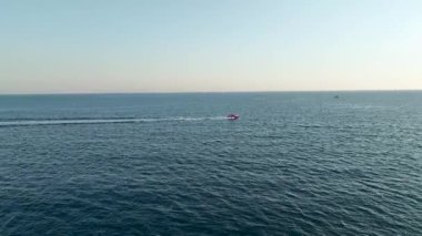 Suyun üzerinde yüzen hızlı bir tekne görüyorsun, altın gün batımına doğru ilerliyor..