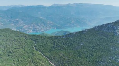 Dağların tepesinde sisli bir orman görüyorsunuz bulutlar yavaşça ağaçların arasında süzülüyor..