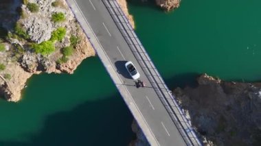 Bir modelin nehir boyunca üstü açık bir araba sürüşünün keyfini çıkarın, büyük, manzaralı bir köprüden geçerken..