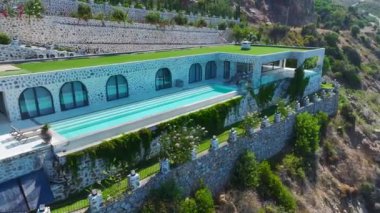 Kayalık sahil şeridinde, okyanus manzaralı parlak mavi bir havuzu olan elit bir villa görün..