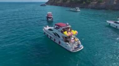 Canlı gök mavisi kıyı şeridi boyunca beyaz yatlarda gerçekleşen heyecan verici parti kutlamalarını izleyin..