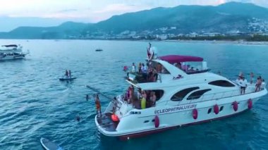 DJ 'e bakın, müzik çalıyor ve kızlar beyaz yatlarda dans ediyor. Gök mavisi kıyı şeridinde demirli..