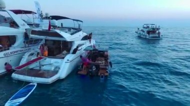 Beyaz yatlarda bir DJ 'in müzik çaldığı ve kızların gök mavisi sahil şeridinde dans ettiği hareketli partiye bakın..