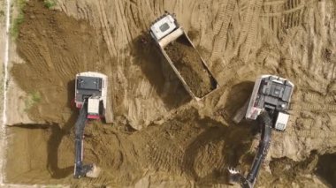 Yukarıdan 4K ile çekilen bir kazı alanında ağır makinelerin ve kamyonların birlikte çalışmasını izleyin..