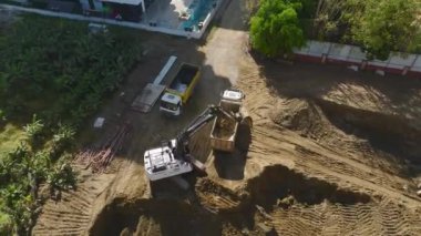 Kazı işlemine bakın, kazıcı toprağı kamyonlara yüklerken, 4K 'da yukarıdan çekiliyor..