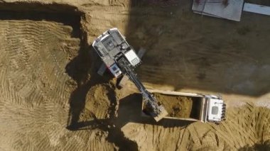 Bir inşaat sahasının dinamiklerini bir kazıcının kamyonlara toprak yüklediği, 4K 'da çekilen.