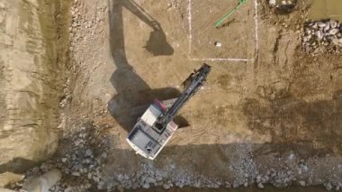 Bir kazı makinesinin ve bir inşaat sahasının temelini hazırlayan kamyonun 4K drone görüntülerini yakalayın..
