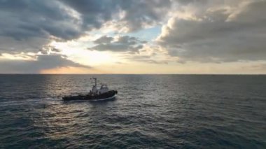 Gün batımında limana giden bir römorkörü takip et, nefes kesen gökkuşağı ve şehir manzarası 4K.