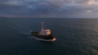 Gün batımında limana varan bir römorkör görün, nefes kesici bir gökkuşağı ve canlı şehir manzarası ile nefes kesici 4K.